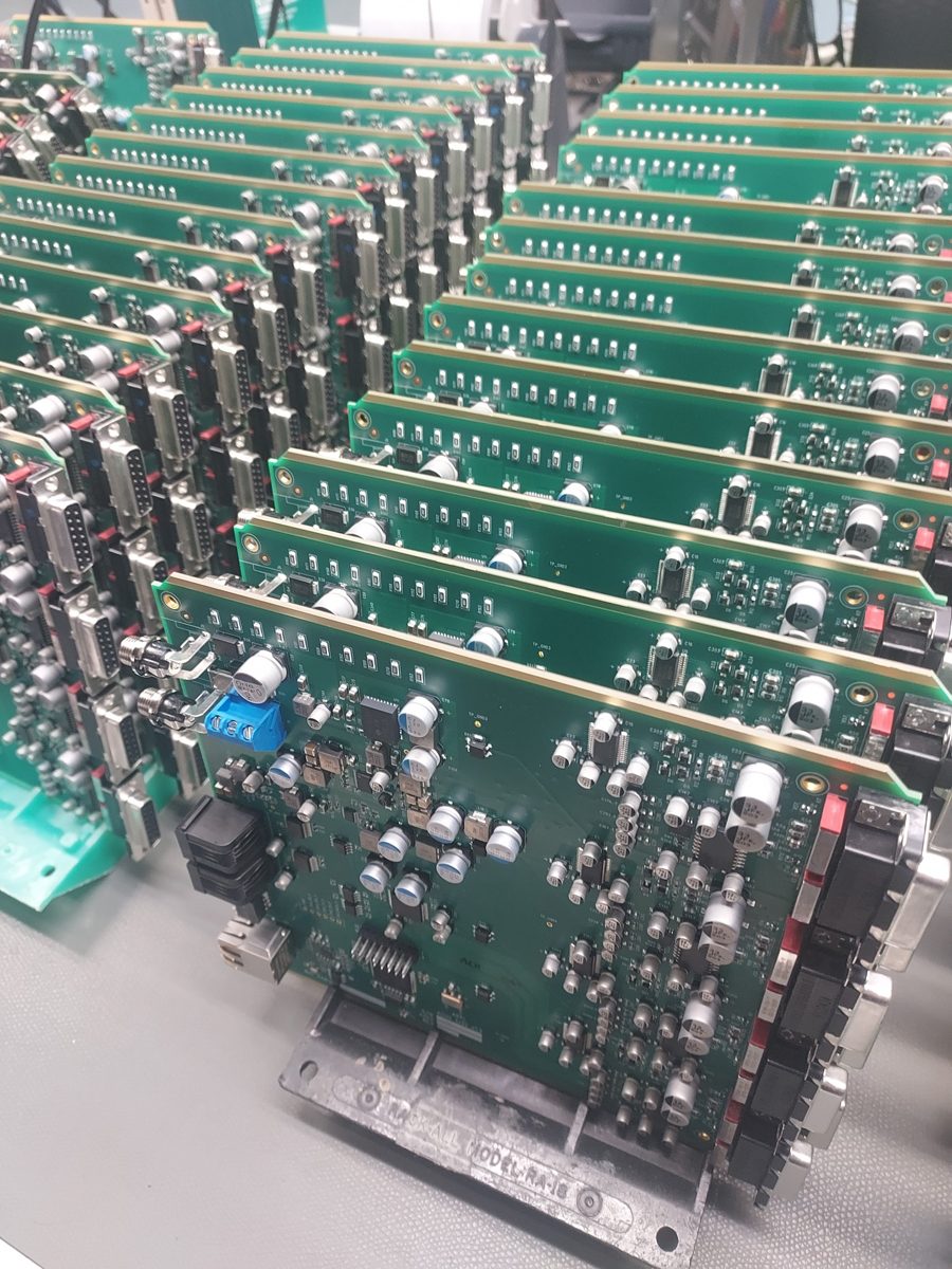 Populated circuit boards standing in a production rack after assembly, showing surface-mount and through-hole components and gold edge connectors.