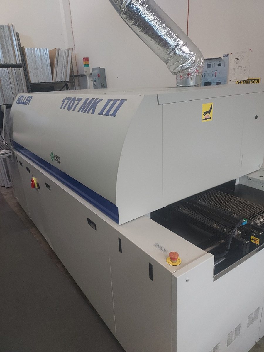 A Heller 1707 Mk III reflow oven on the surface-mount line, with extraction ducting and the conveyor entry visible.