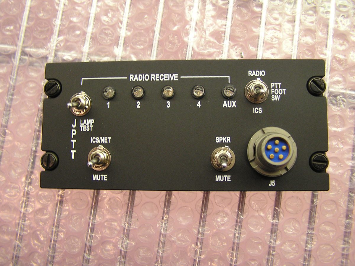 A completed radio and intercom control panel with an anodized faceplate, engraved legends, toggle switches and a circular military connector.